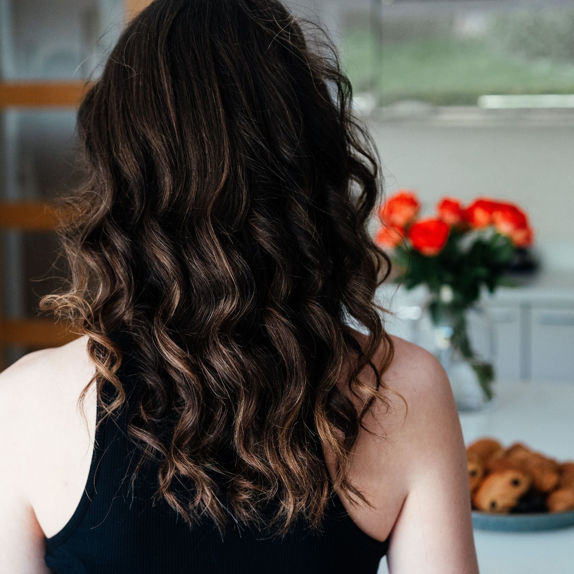 Woman with long wavy healthy looking hair with a flowers and breakfast pastries in front of her