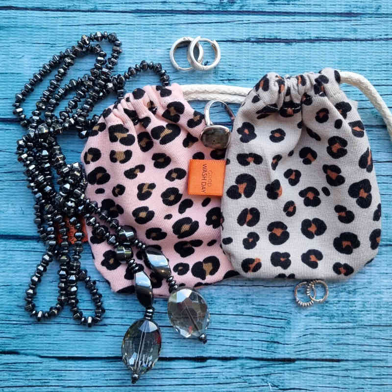 Handmade in the UK, Good Wash Day leopard print drawstring pouch with jewelry and beaded necklaces on a blue wooden background.