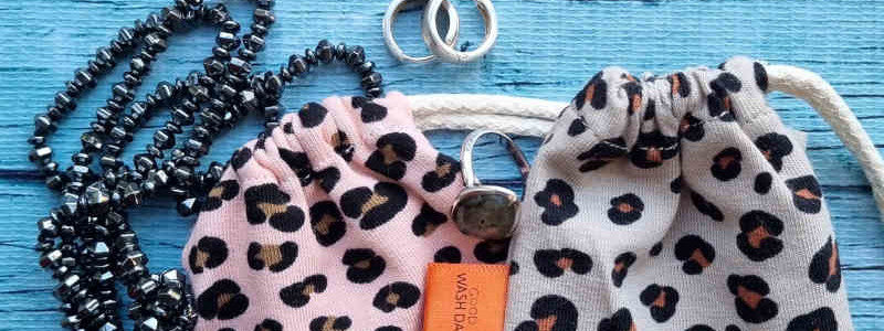 Three small drawstring bags: one black, one orange, and one with a leopard print pattern, each with a brown string and a small orange tag.