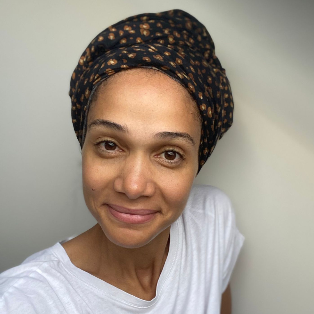 Woman wearing a patterned hair towel and white shirt against a plain background