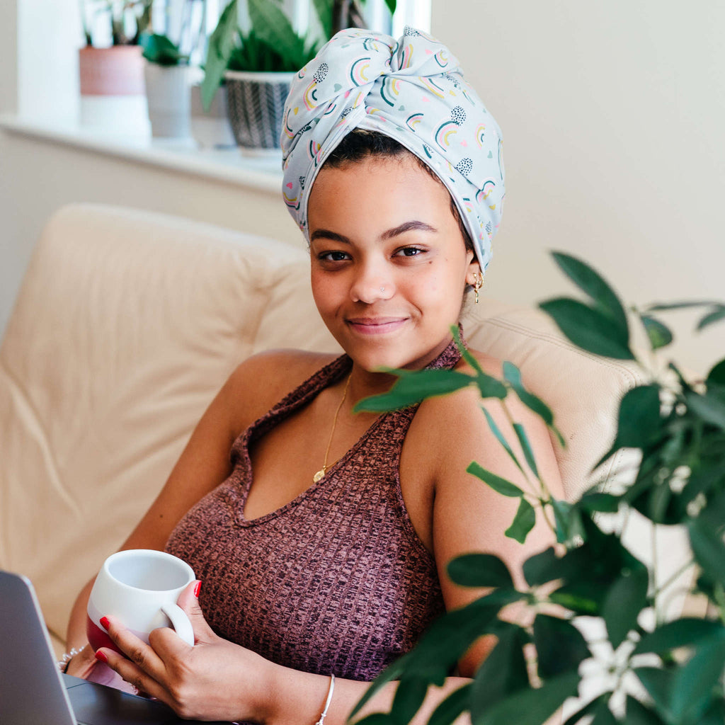 Woman with a headscarf sitting comfortably with a cup and a laptop, surrounded by houseplants.