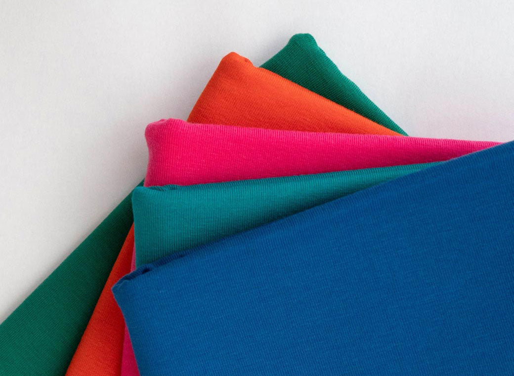 A stack of folded Good Wash Day hair towel wraps in bright colors, including blue, teal, pink, orange, and green, arranged diagonally against a plain white background.