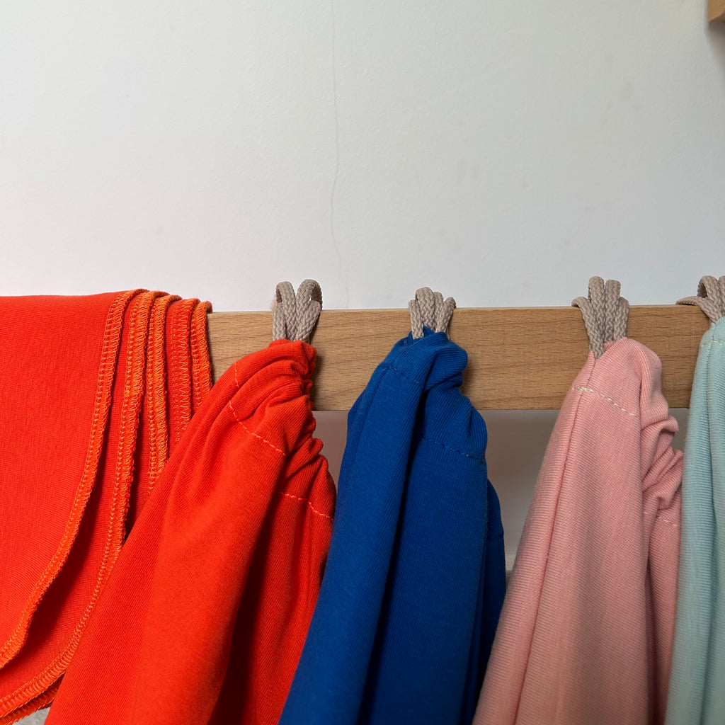 Colorful Good Wash Day reusable face cloths hanging neatly on wooden hooks against a white wall.