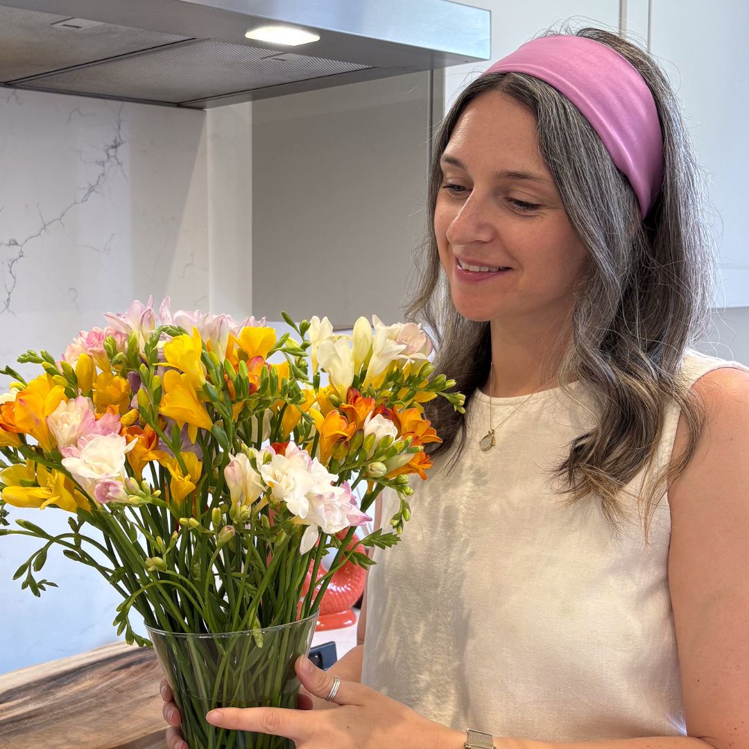 Woman wearing violet organic jersey cotton headband whilst looking at a vase of colourful flowers – Good Wash Day