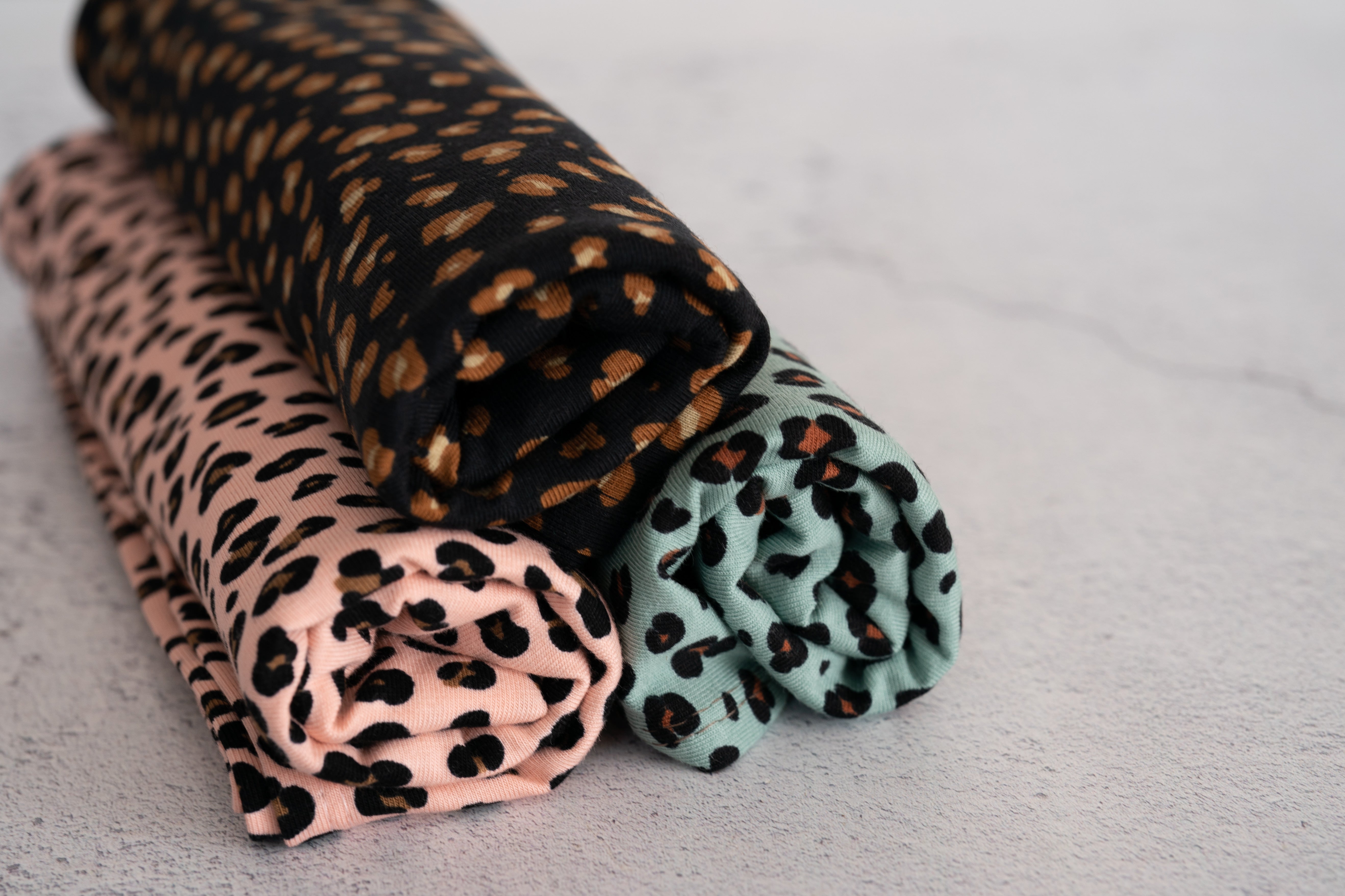 Three leopard print organic jersey cotton hair towels in pink, mint and black, rolled up