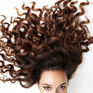 Close-up of a woman displaying lush, long brown curly hair on a white background, highlighting healthier and stronger hair—perfect for a Good Wash Day.