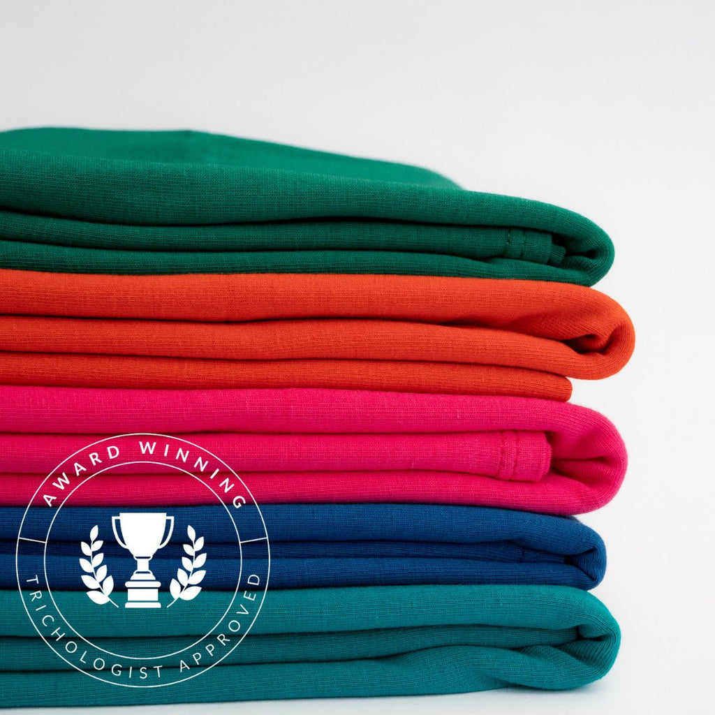 A stack of neatly folded colorful organic cotton The XLs t-shirts with an 'award-winning psychologist approved' badge in the corner from Good Wash Day.